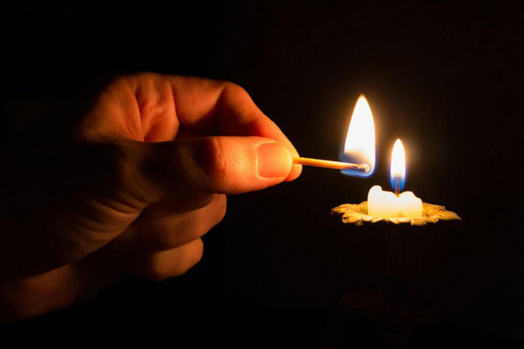 por-que-deus-permite-sofrimento (3) uma mão que ascende uma vela em sinal de oração