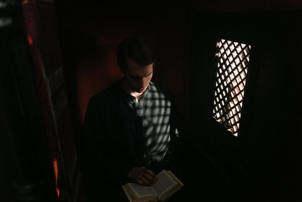 maldicao-hereditaria (2) padre dentro de um confessionário e uma Bíblia nas mãos
