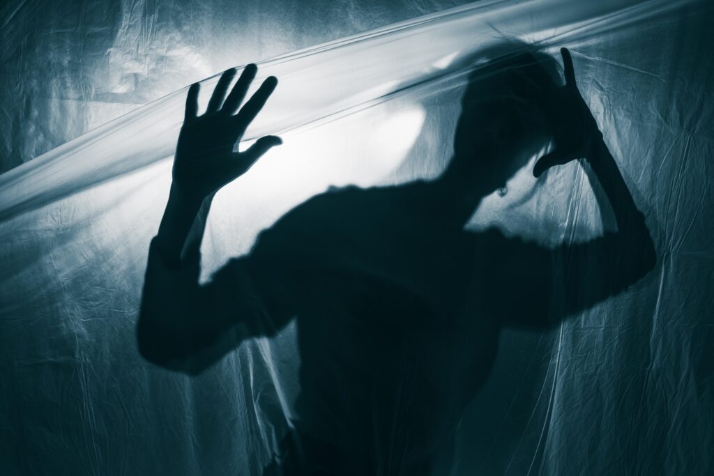 pecado-mortal Silhueta de uma pessoa presa atrás de um plástico, simbolizando o isolamento e a morte espiritual causados pelo Pecado Mortal.