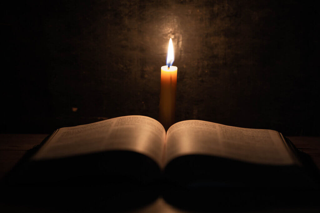 Bible and candle on a old oak wooden table. imagem de uma bíblia aberta em cima de uma mesa e ao fundo uma vela acesa.