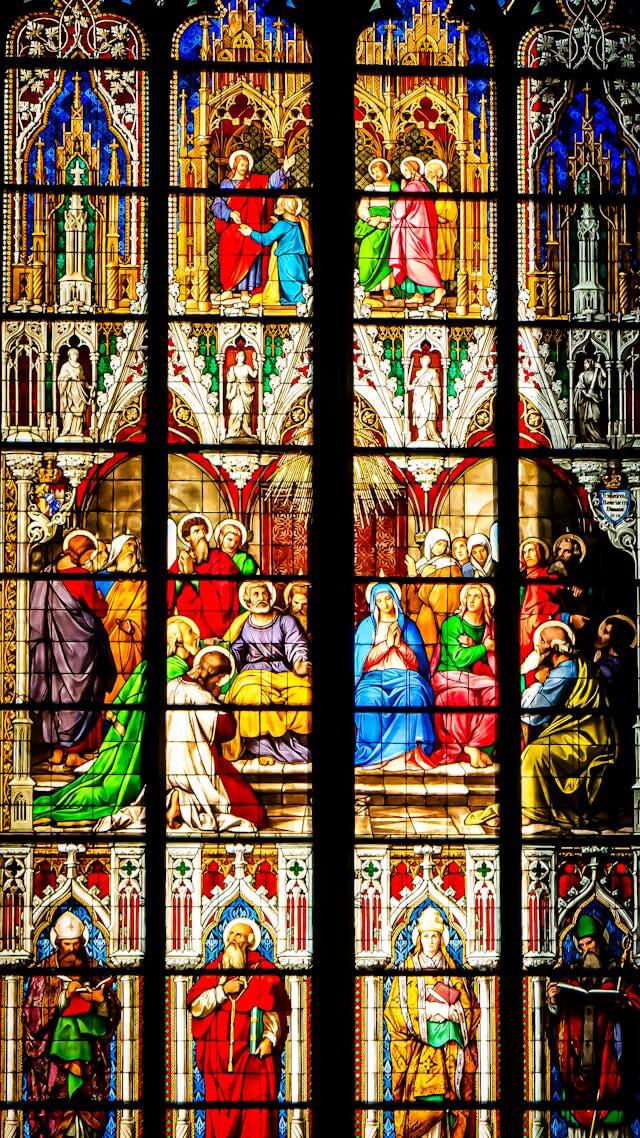 Vitral gótico detalhado e colorido dividido em registros horizontais. No topo, figuras divinas representam o Dogma; no centro, apóstolos e santos ilustram a Doutrina; na base, bispos e fiéis simbolizam a Disciplina e a vida da Igreja. A luz que atravessa o vidro une os três níveis em uma única estrutura de fé.